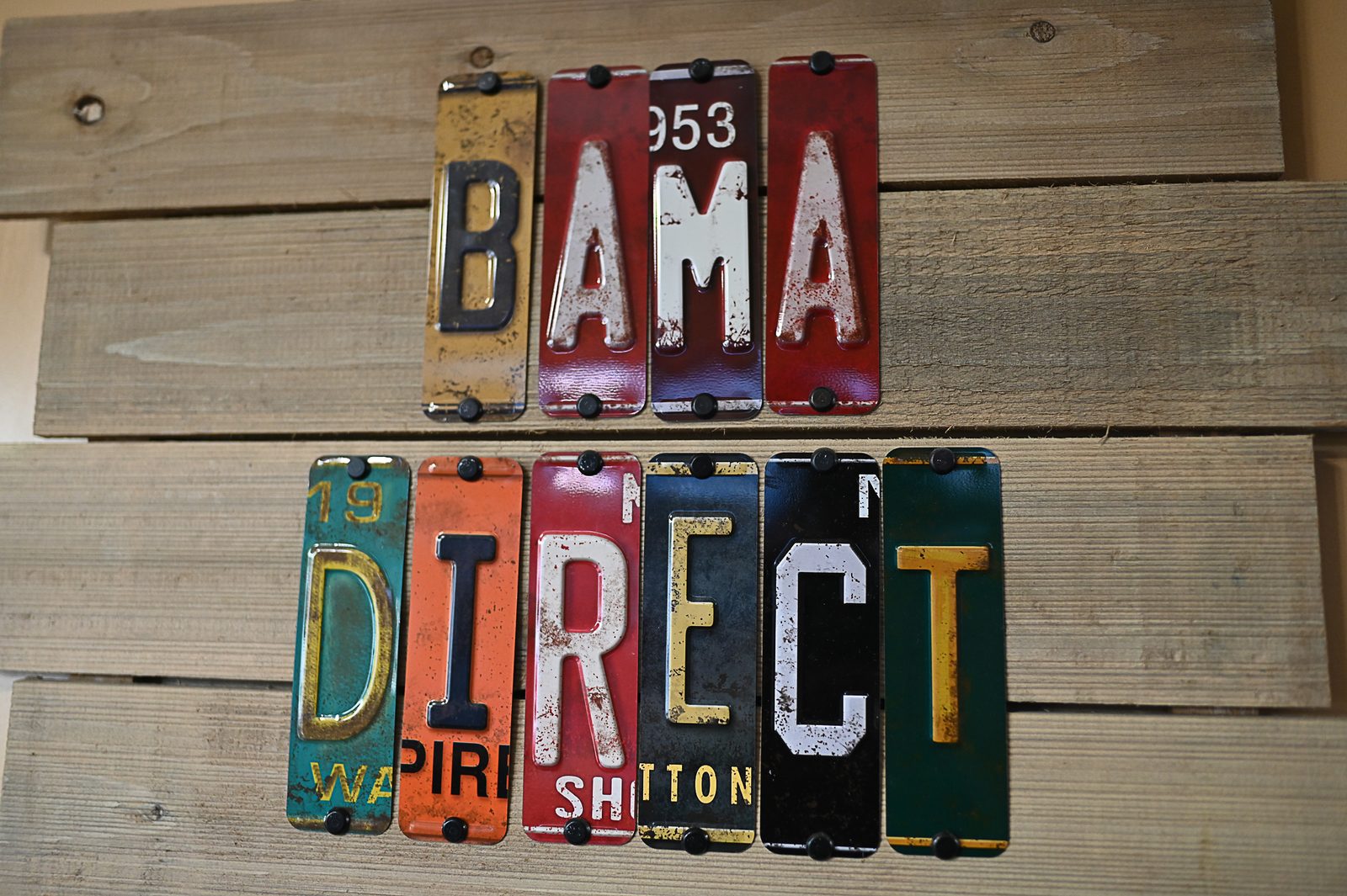 Vintage Alabama license plates arranged on weathered wood spelling Bama Direct