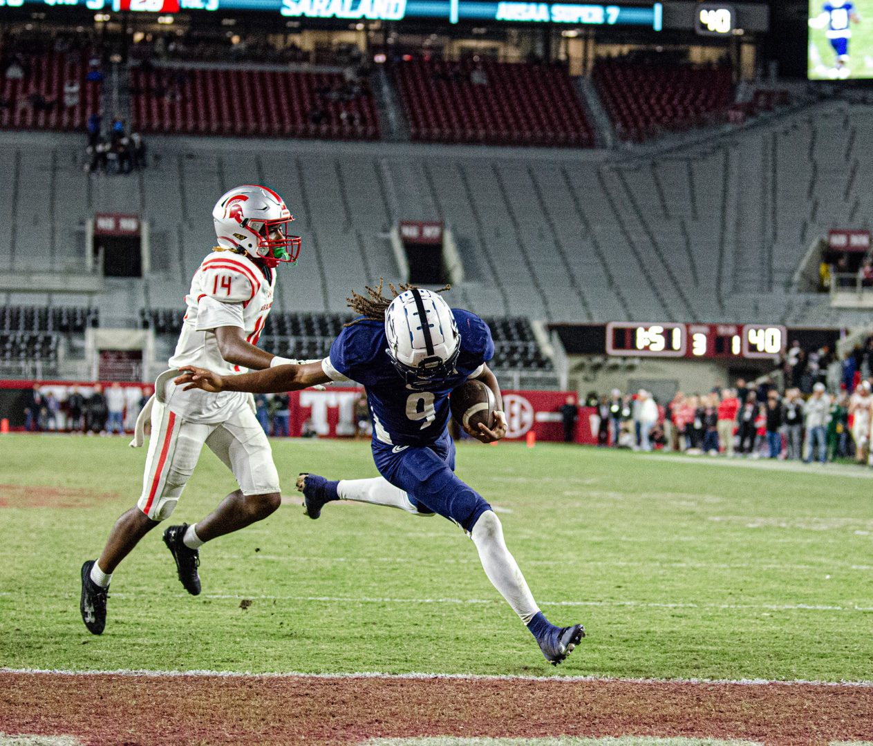 Receiver hauling in a pass with a defender closing in a college stadium