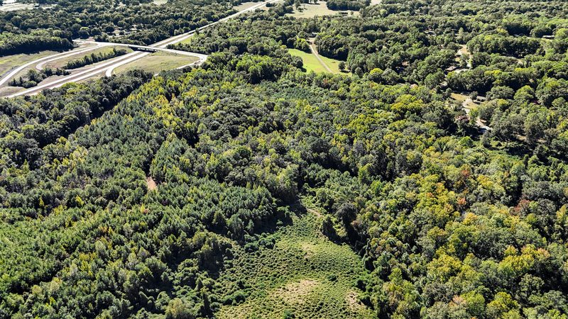 Aerial photo of wooded land with a road and open pasture in the distance