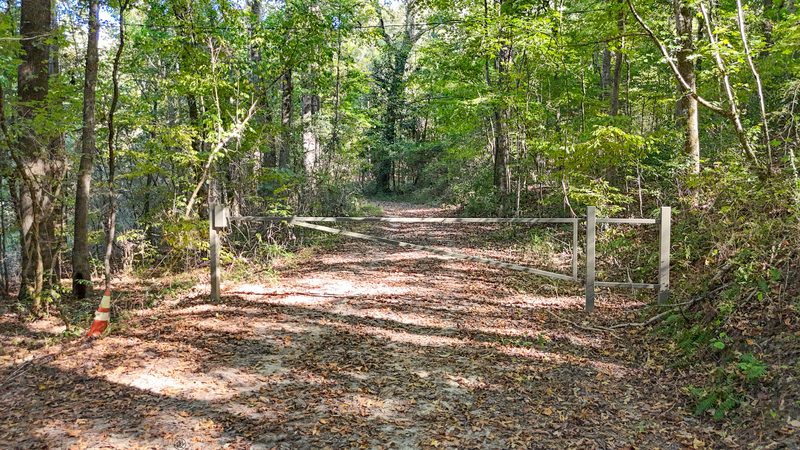 Gated dirt trail leading into the woods from the road